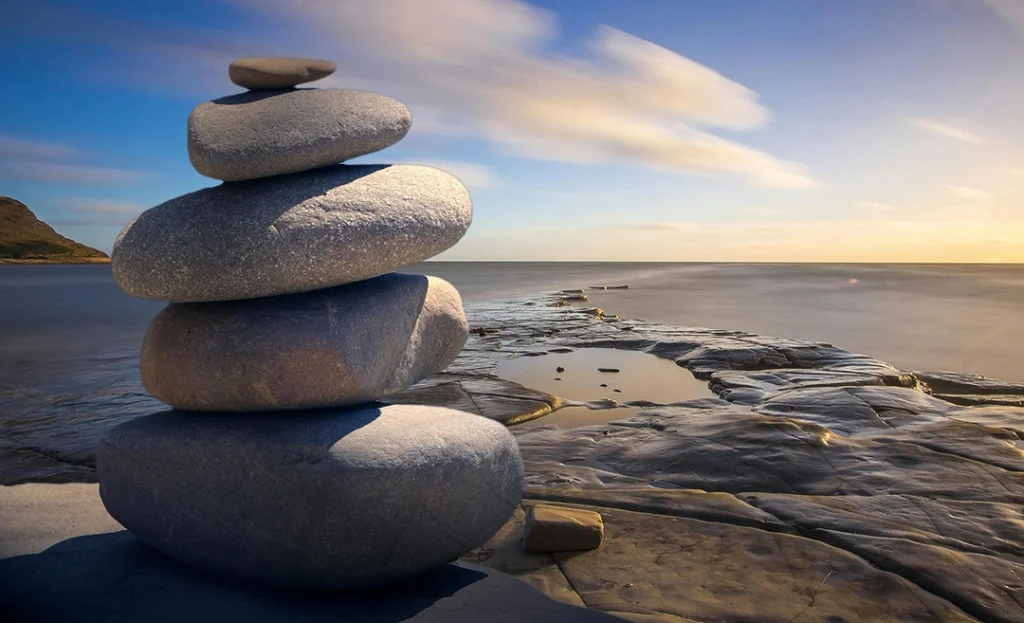 Pilas de piedras equilibradas junto al mar en un paisaje sereno al atardecer.